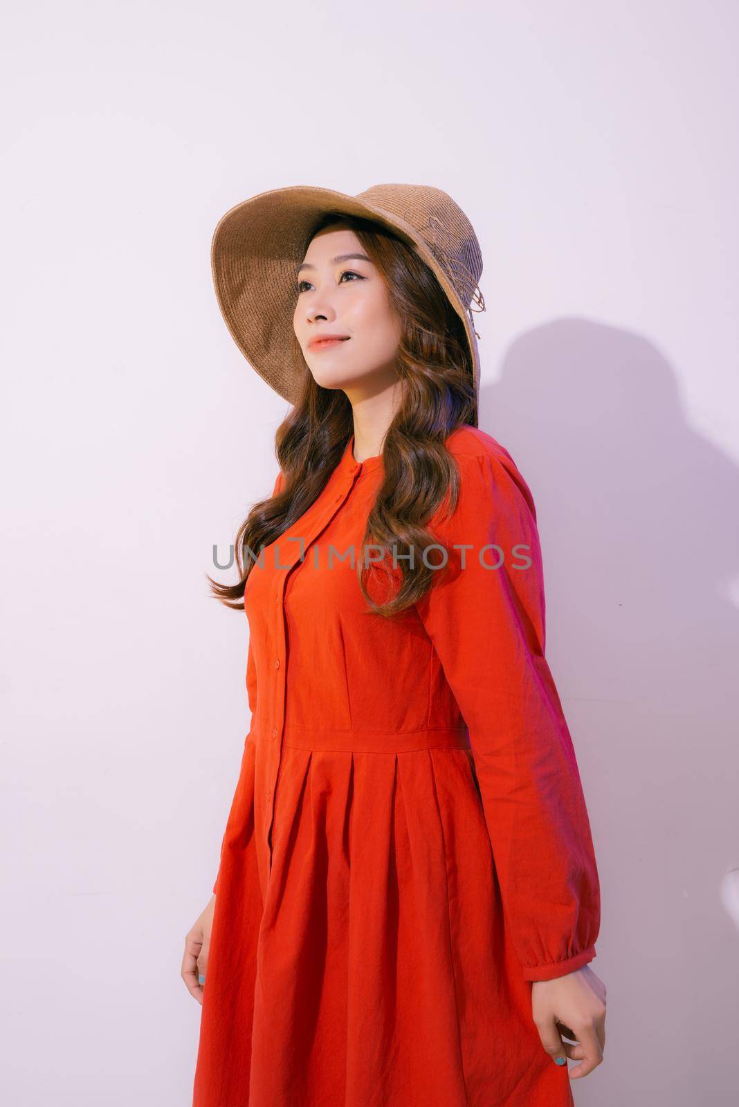 Portrait of an Asian woman wearing a wide-brimmed hat and summer clothes isolated on pink background