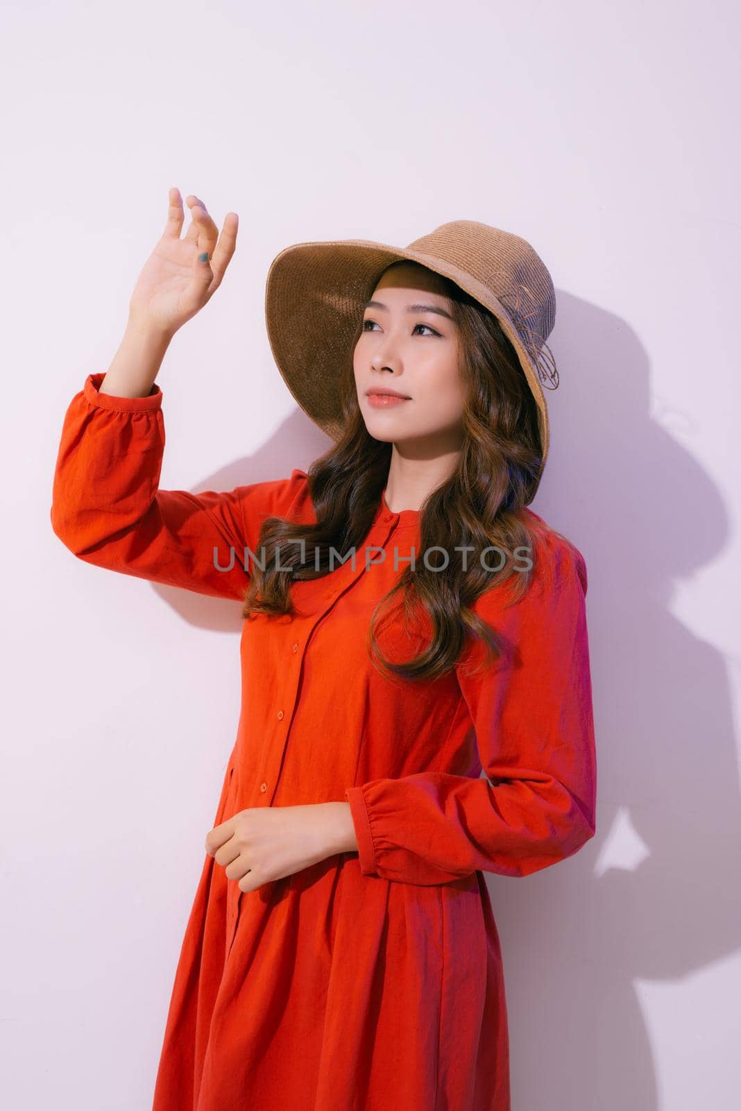 Portrait of a smiling attractive woman in summer dress and hat posing while standing and looking at camera isolated over pink background