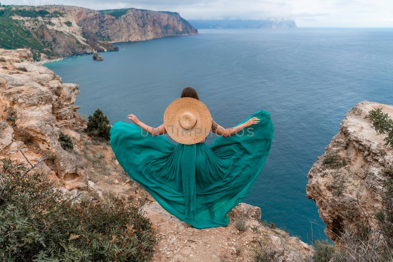 A beautiful girl in a green dress runs to the sea, against the background of large rocks and the sea by Matiunina