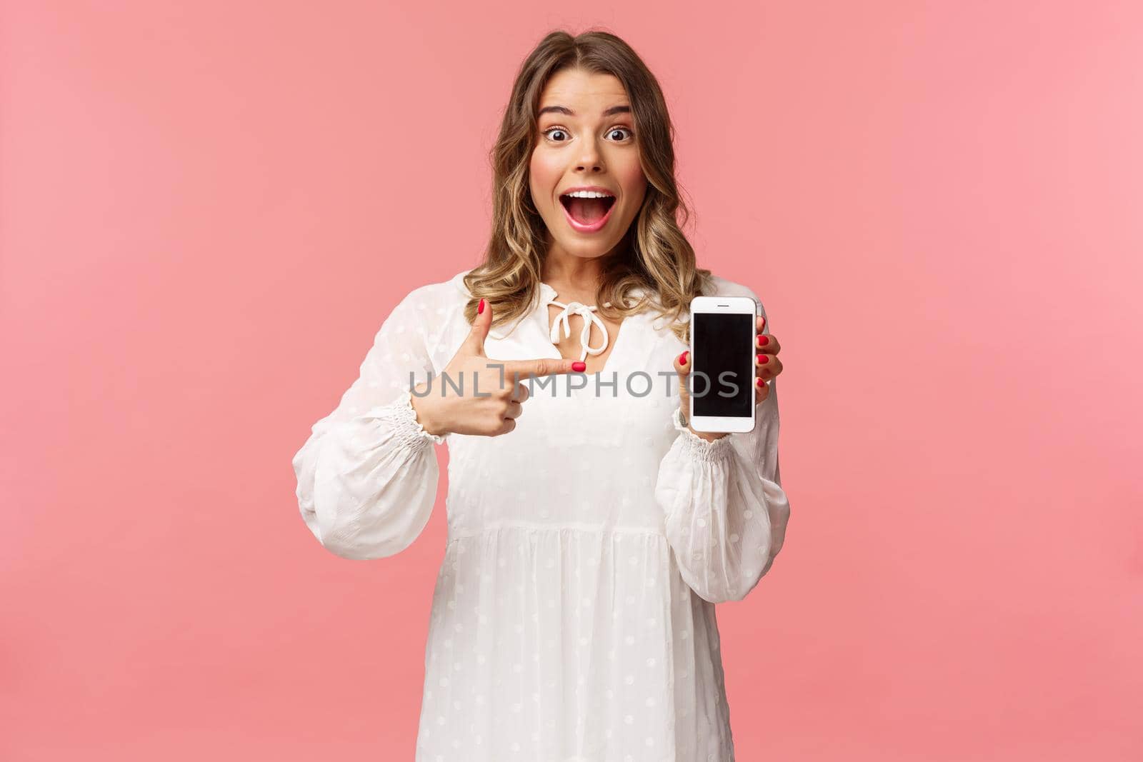 Portrait of impressed, excited young blond woman showing something awesome on display, pointing mobile phone screen and smiling astonished, brag with her recent match on dating app.