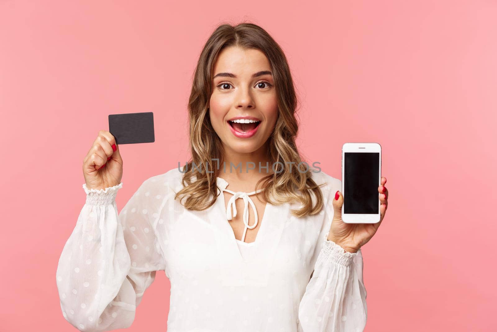 Finance, shopping and technology concept. Close-up portrait of excited blond attractive girl in white dress, showing credit card and mobile phone, advertise online store, smartphone app.