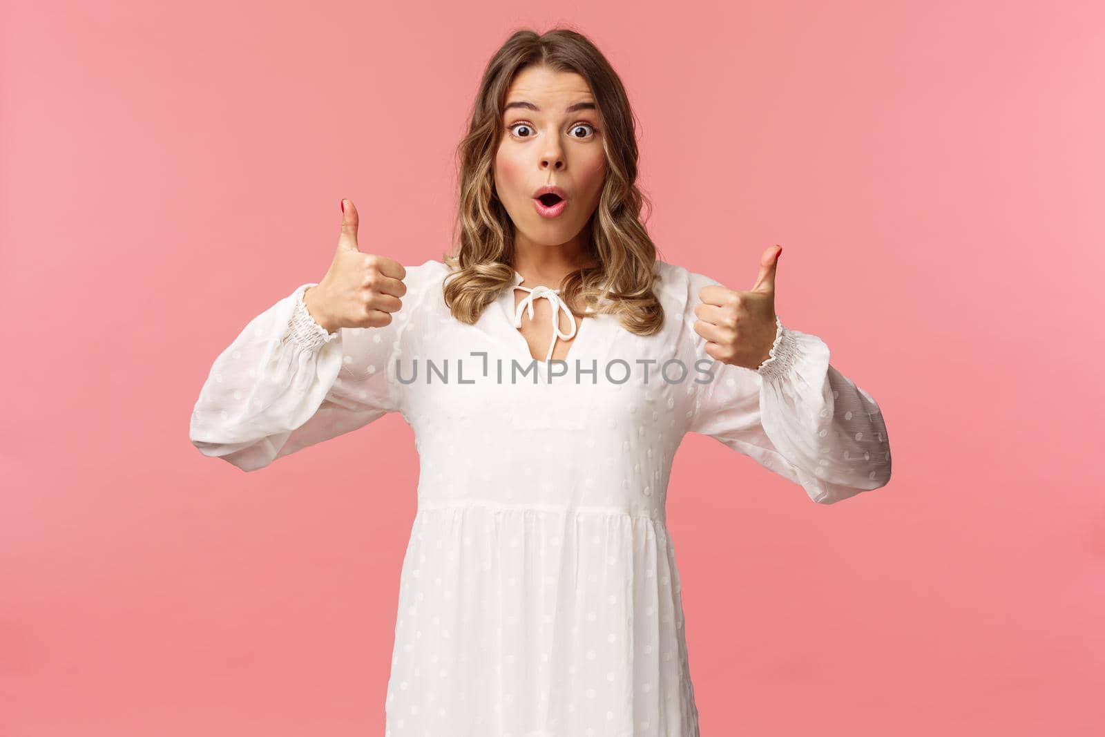 Portrait of amazed, excited blond young girl in white cute dress, open mouth say wow astonished and fascinated, show thumbs-up like and approve, beaing satisfied, pink background by Benzoix