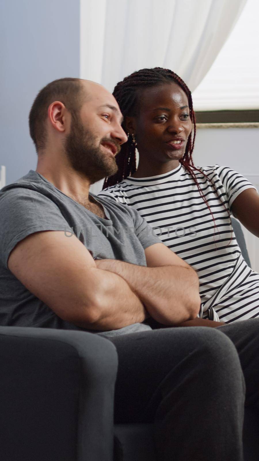Interracial partners using video call on smartphone in living room. Cheerful multi ethnic couple chatting on online conference via internet for remote communication at home on couch