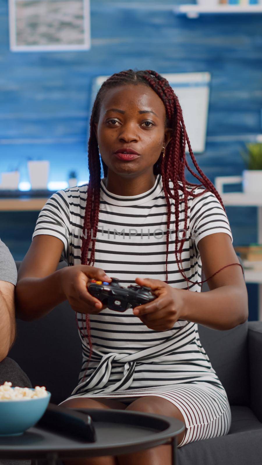 POV of young interracial couple using technology for enjoyment at home. Married multi ethnic man and woman playing video game on TV console with controllers on living room couch