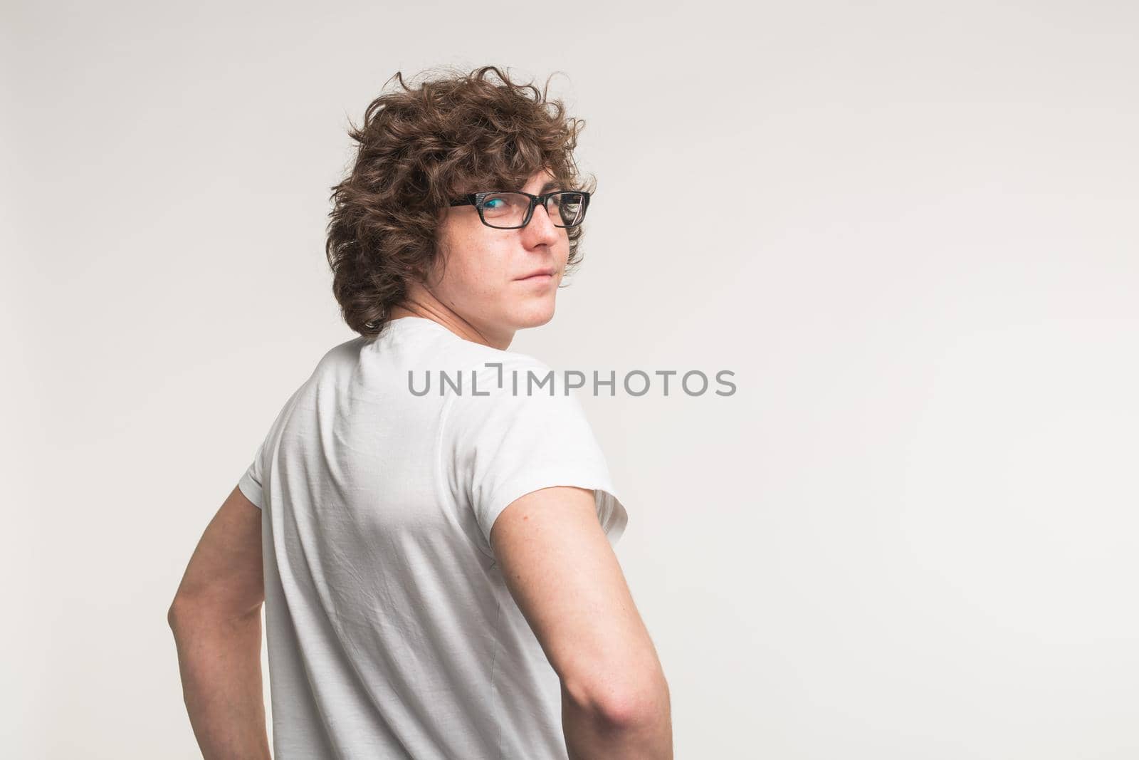 Young man in white t-shirt and glasses turning back at the camera in studio