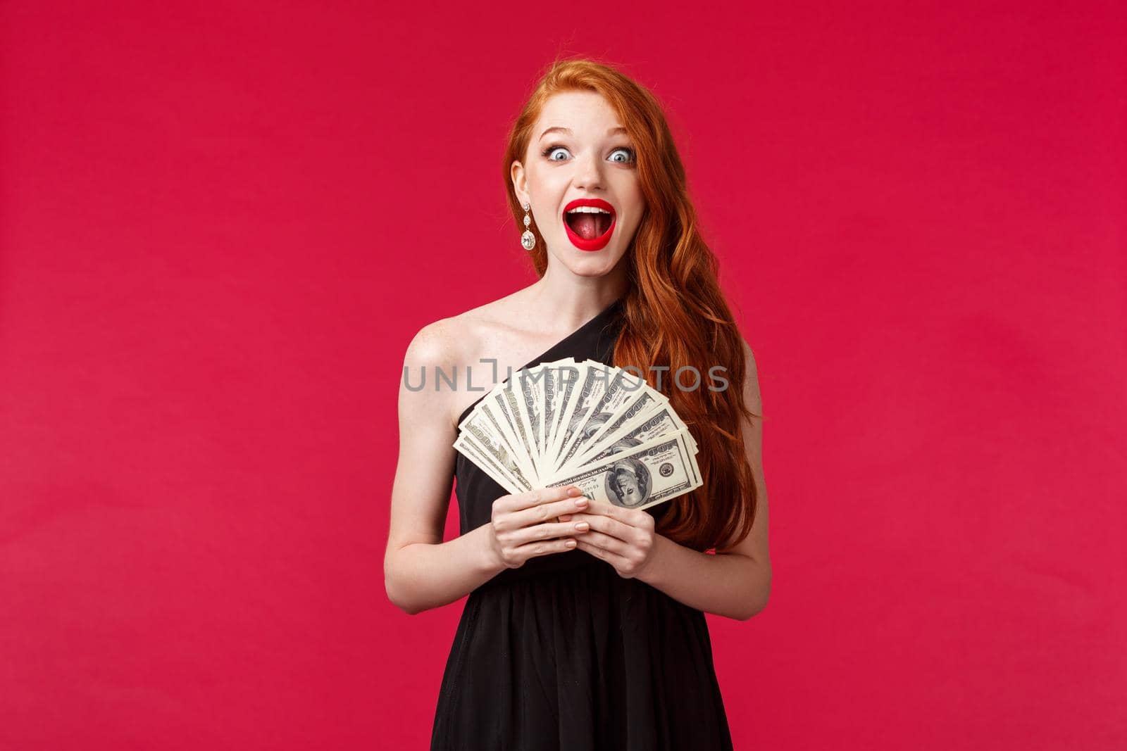 Luxury, beauty and money concept. Surprised and excited gorgeous redhead woman in black dress, screaming amazed and pleased, receive cash prize, stare impressed, feel lucky triumphing.
