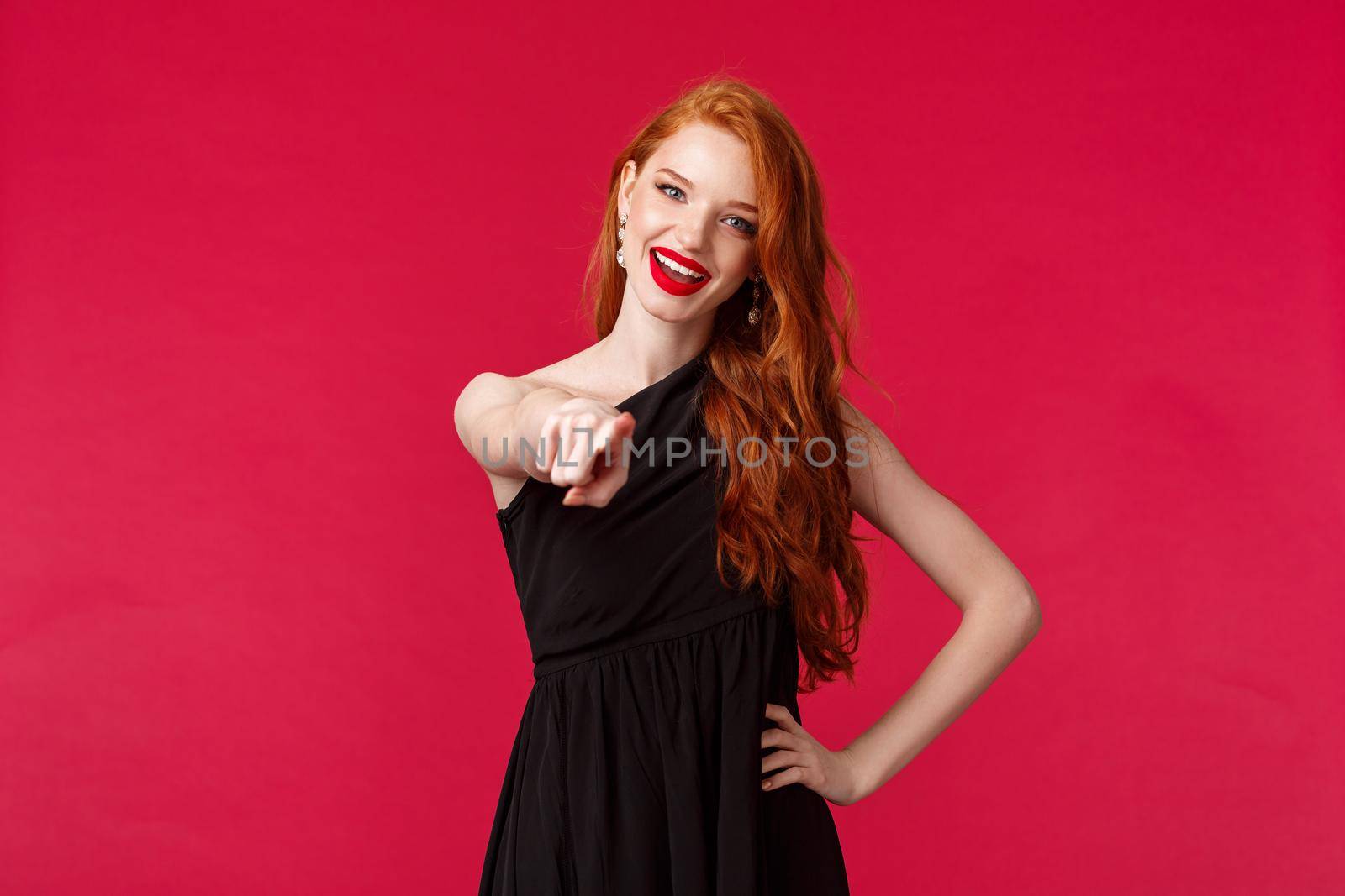 Fashion, luxury and beauty concept. Portrait of sassy and assertive redhead female in black dress and evening makeup, pointing at camera inviting you to party, encourage have dance together.