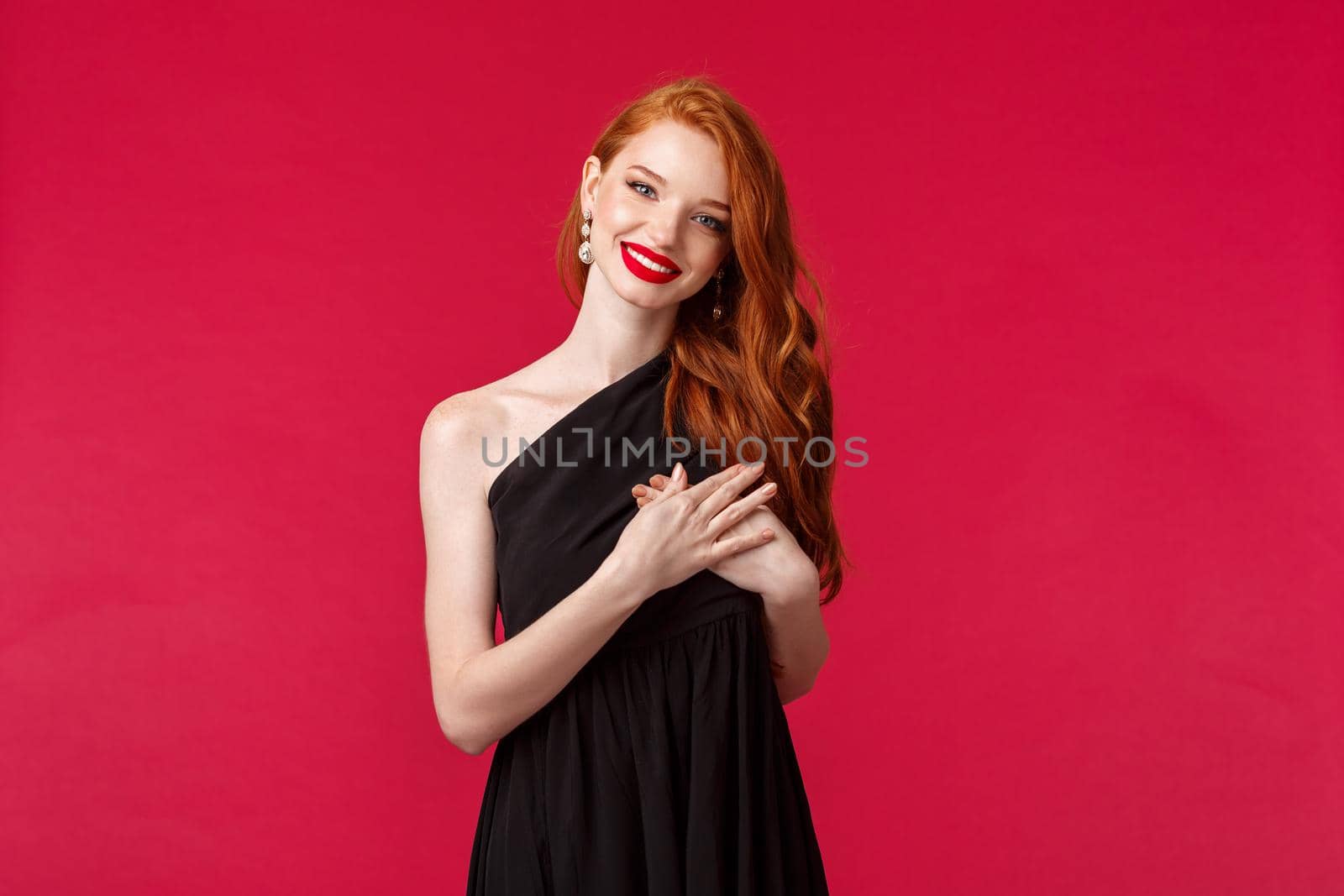 Fashion, luxury and beauty concept. Elegant good-looking redhead woman in black dress, with red lipstick and luxurious outfit, tilt head and smiling thankful, hold hand on heart touched with praises by Benzoix