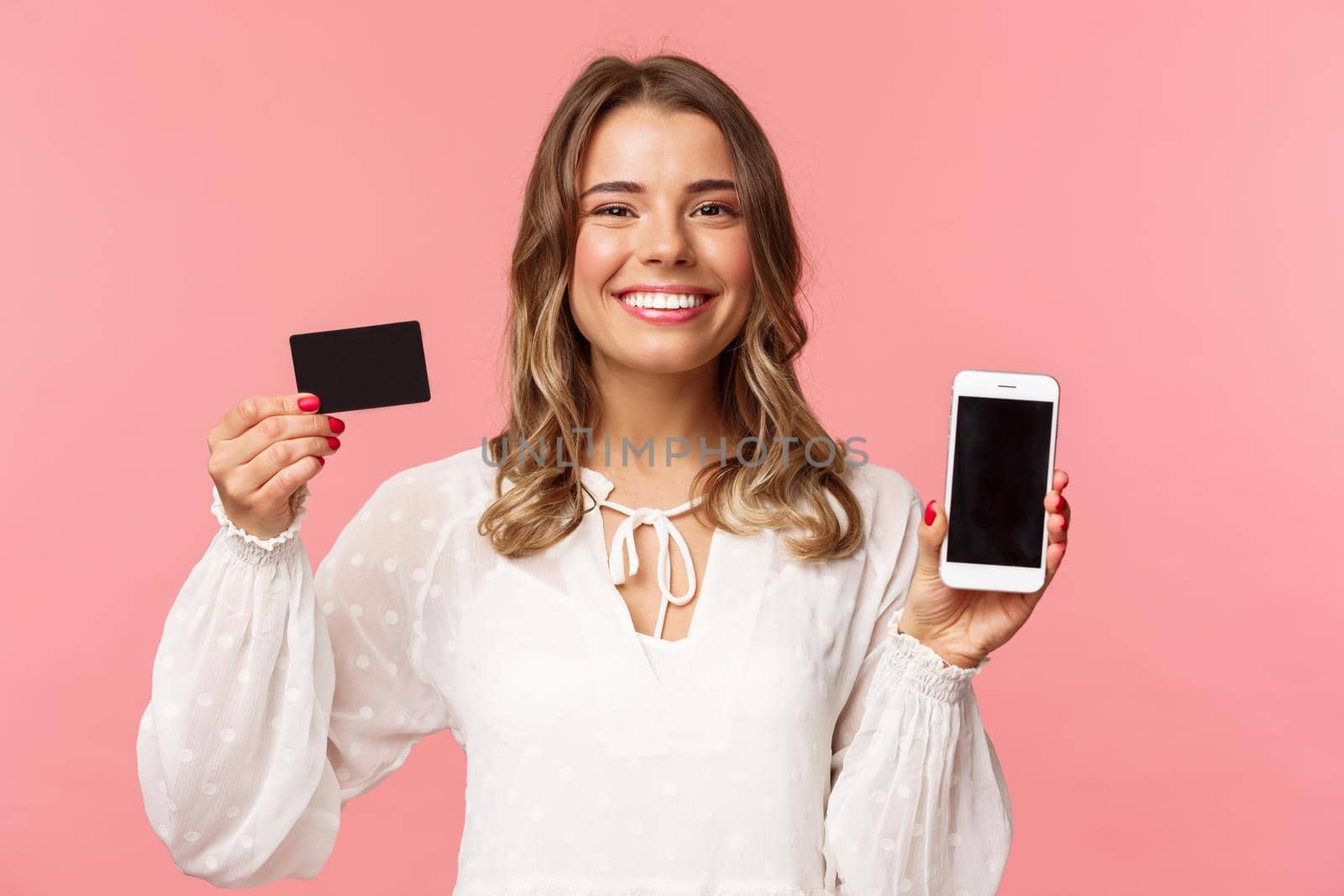 Finance, shopping and technology concept. Close-up portrait of cheerful, romantic blond cute girl in white dress, holding credit card and mobile phone, showing smartphone display, application promo by Benzoix
