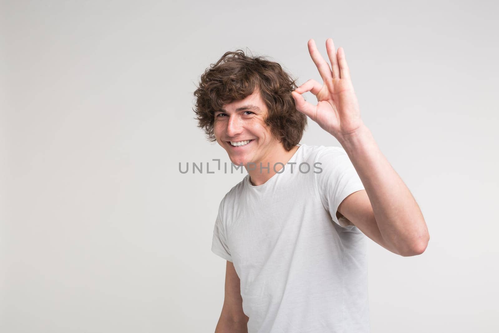 young handsome freckled man on white background showing ok sign