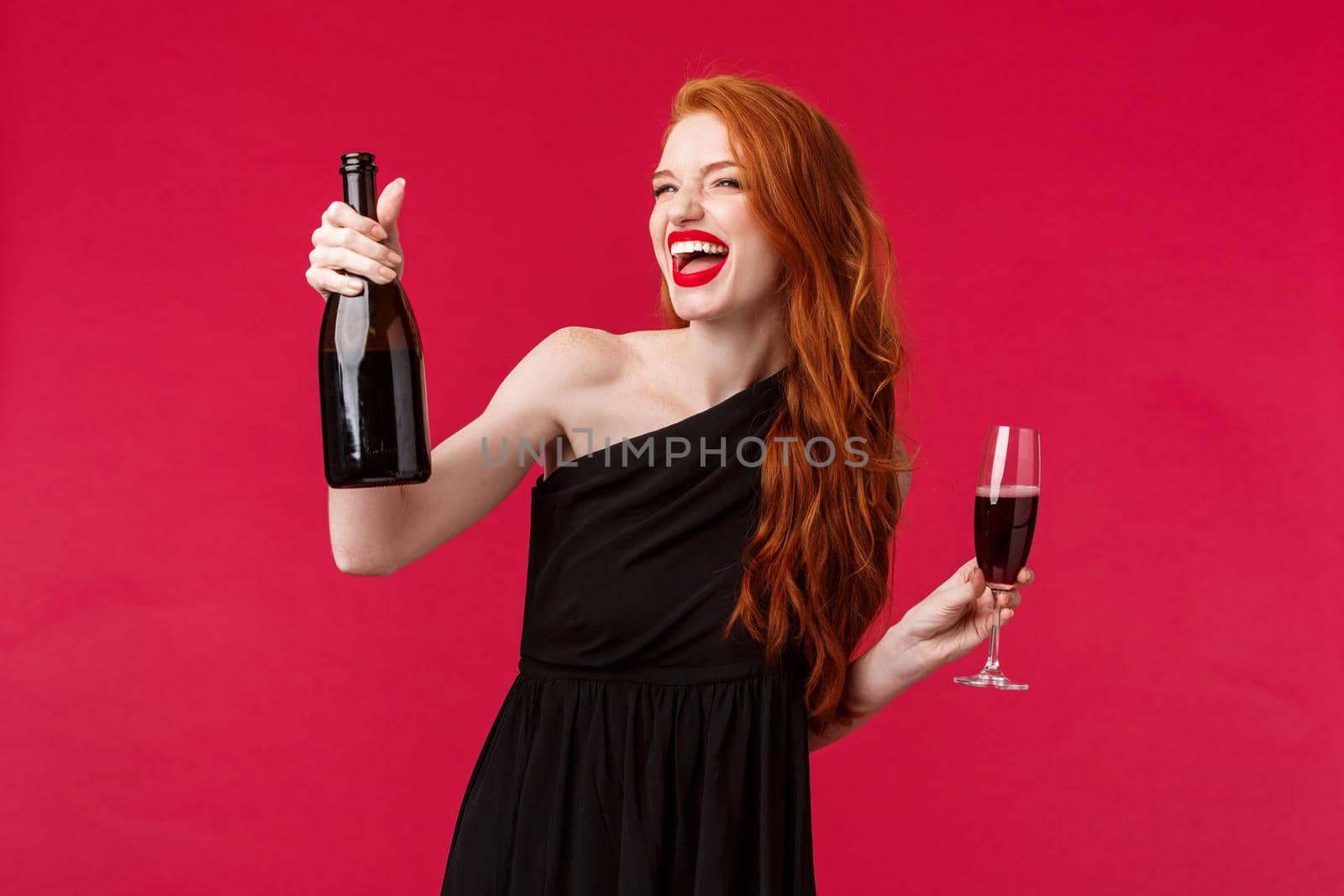 Carefree excited beautiful redhead woman celebrating night out with girlfriends, partying on birthday or holiday, holding bottle champagne saying cheers drink from glass, look away satisfied.