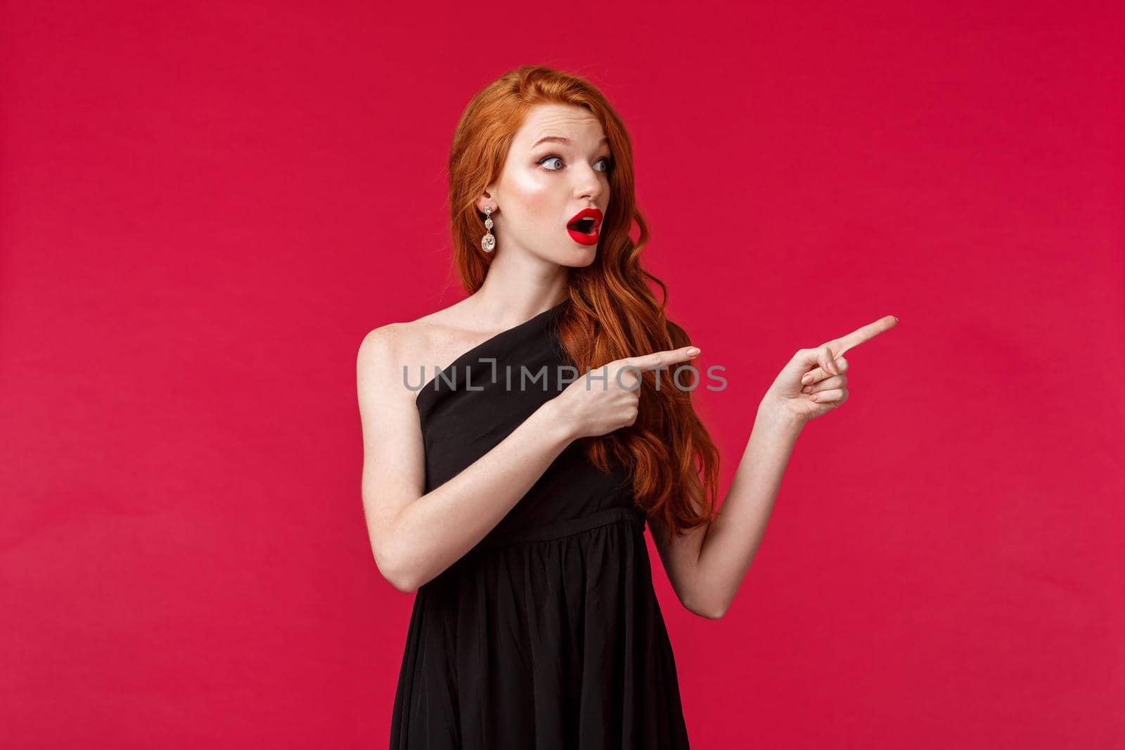 Celebration, events, fashion concept. Surprised elegant and pretty redhead woman, ginger hair, wear beautiful black evening dress, looking and pointing right, turn attention at interesting promo.