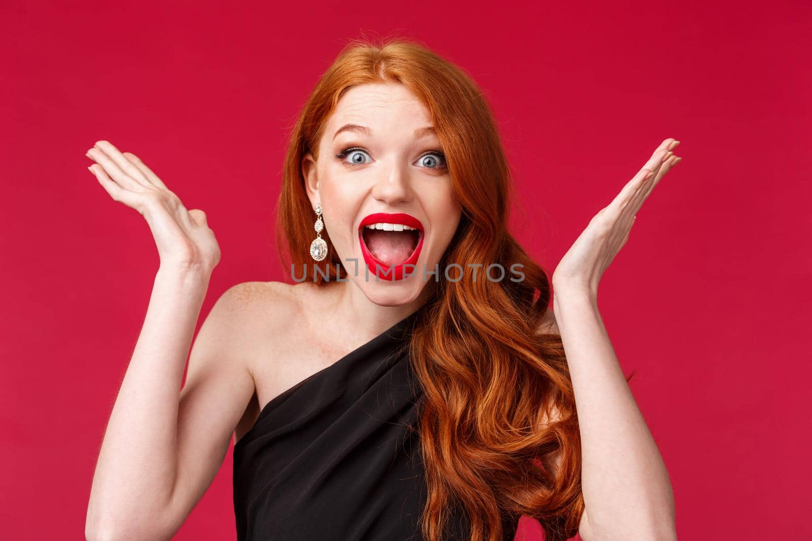 Celebration, emotions and beauty concept. Close-up portrait of happy cheerful redhead woman winning, triumphing over excellent great news, raise hands up and scream joyful, red background.