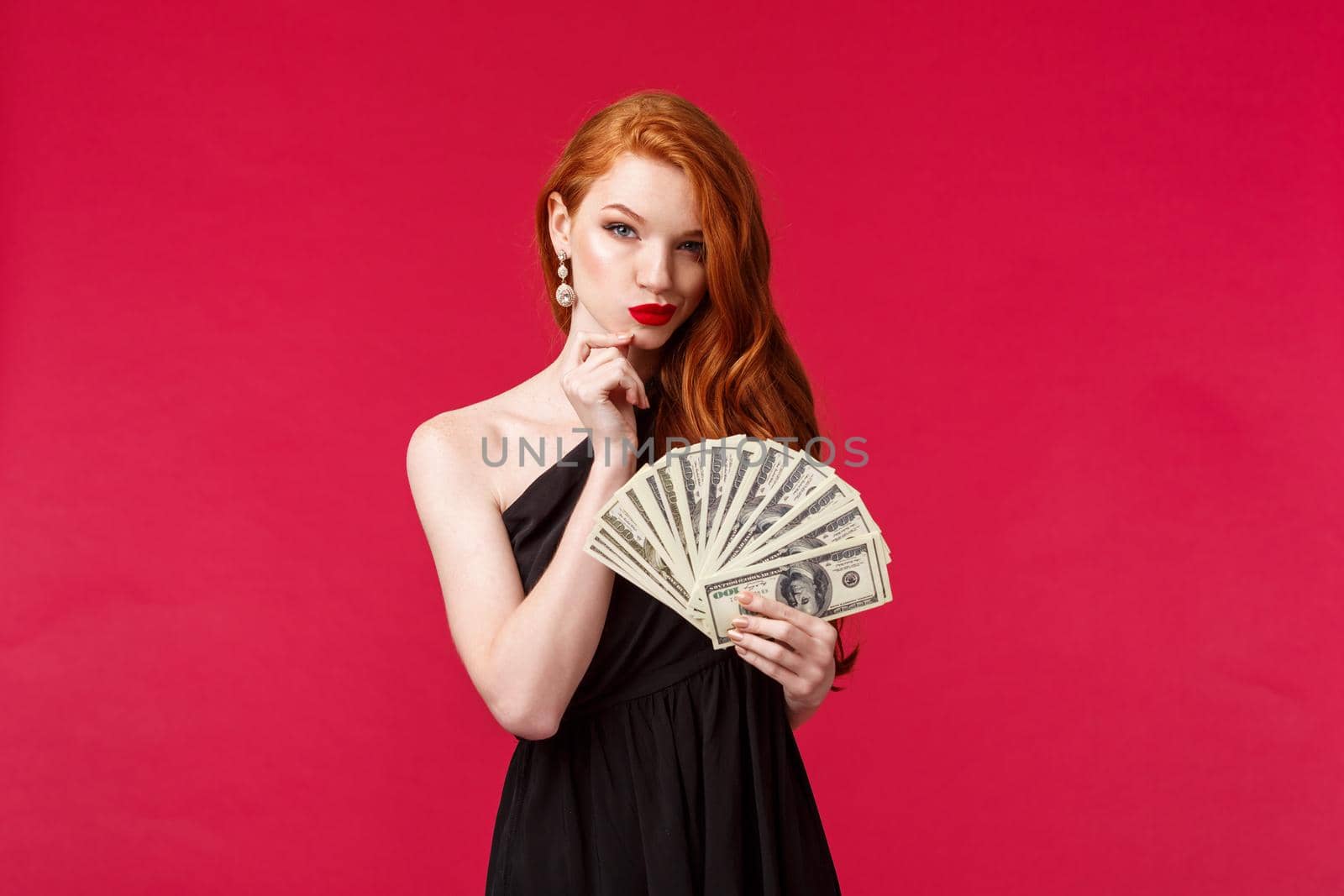 Luxury, beauty and money concept. Portrait of dubious and scheming good-looking young redhead woman in stylish black dress have interesting idea what buy on this cash dollars.