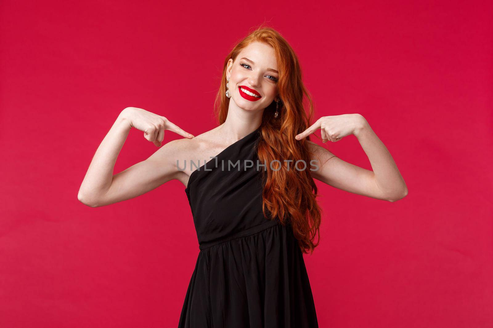 Fashion, luxury and beauty concept. Portrait of confident sassy redhead female in elegant black dress, wear makeup, pointing herself proudly, telling own achievement, red background.