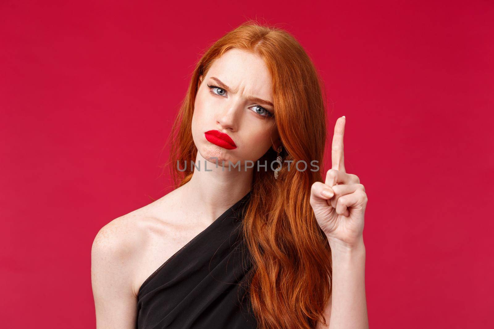 Close-up portrait of displeased moody redhead pretty girlfriend have one condition, frowning disappointed shaking finger as scolding someone, forbid or refuse, standing red background.