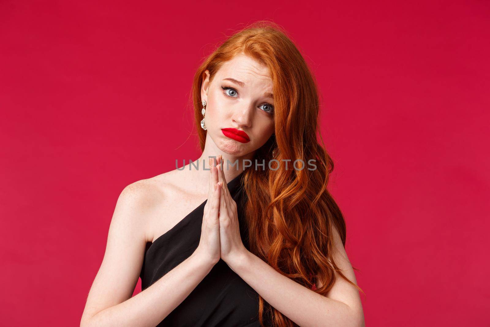 Close-up portrait of gloomy clingy attractive redhead girlfriend in black background asking for something, say please with cute silly face, pouting begging for help, hands pressed together in pray.