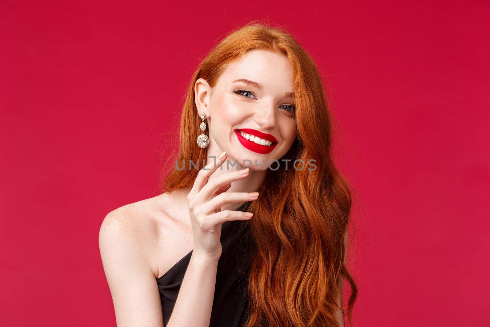 Close-up of happy gorgeous redhead woman with earrings, red lipstick and evening black dress, gently touching her jawline and beaming smile at camera cheerful, enjoying celebration, party concept by Benzoix