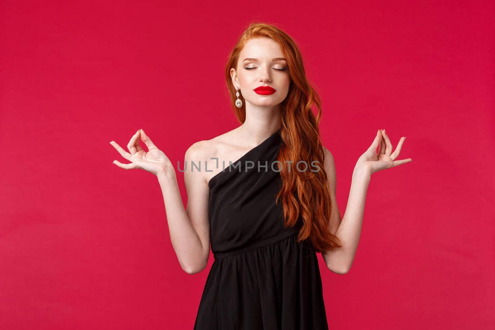 Keep calm and be queen of night. Relaxed and peaceful young beautiful redhead woman in black dress meditating, getting ready for performance, hold hands in lotus nirvana pose, wear black dress.