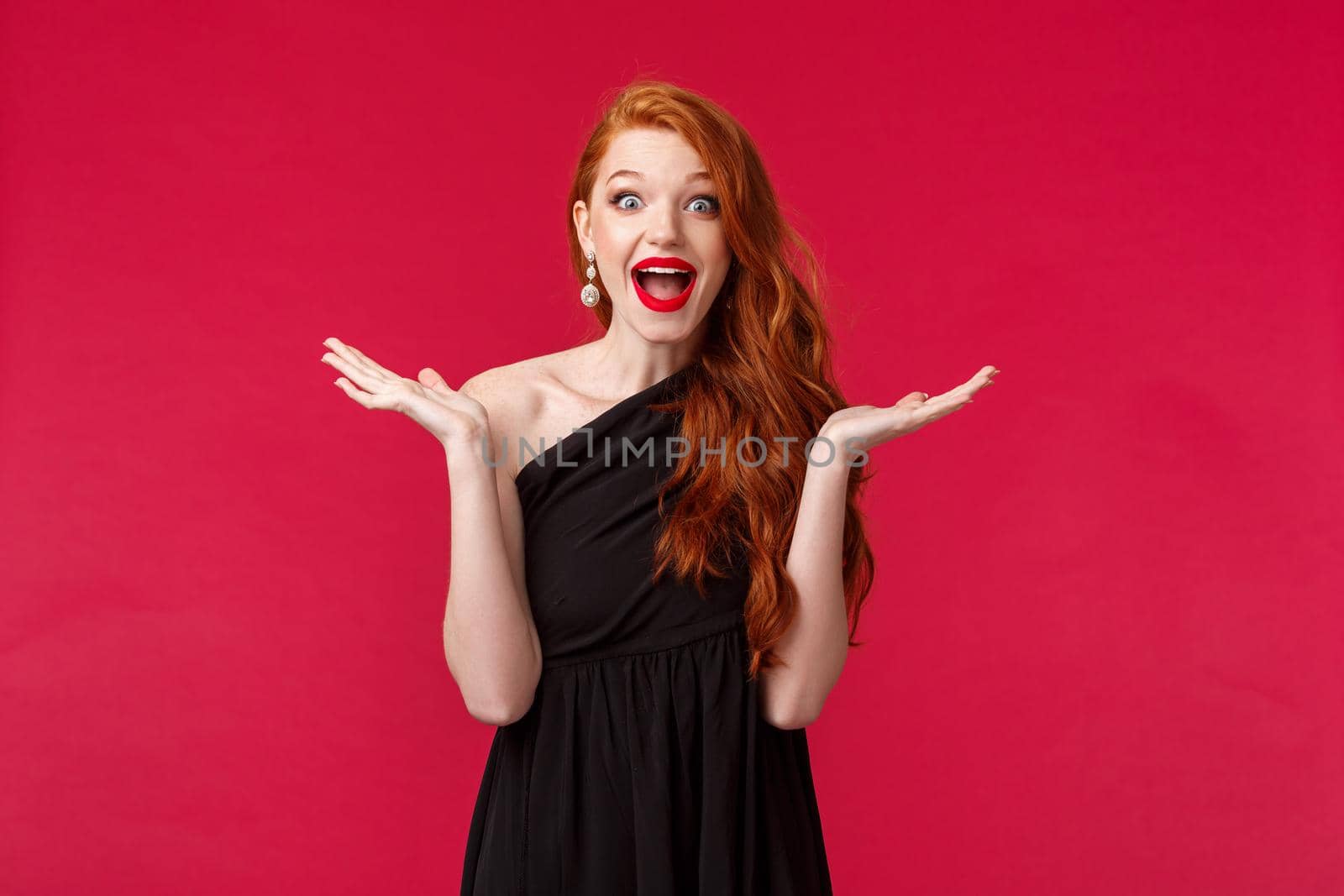 Fashion, luxury and beauty concept. Portrait of happy and surprised excited redhead woman react to unexpected pleasant guest showing-up her party, raise hands sideways and smiling, black dress by Benzoix