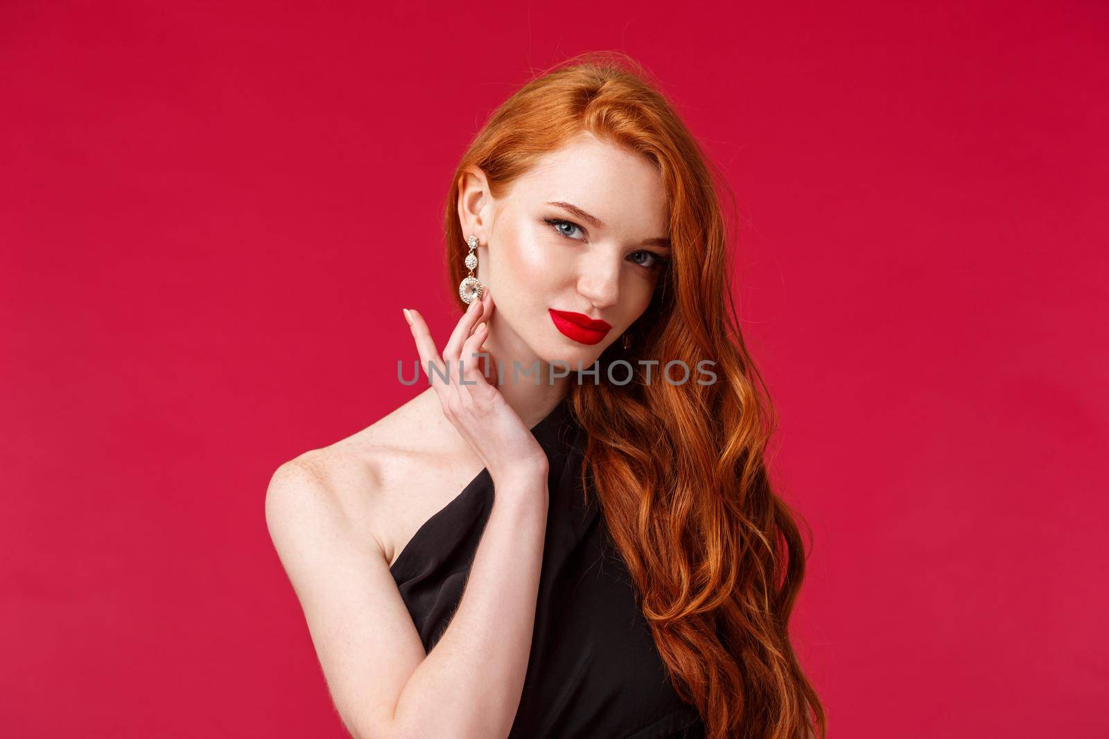 Close-up portrait of sensual seductive redhead woman with red lipstick, touching earring coquettish look camera, slightly smiling as flirting with person on party, wear black dress, red background by Benzoix