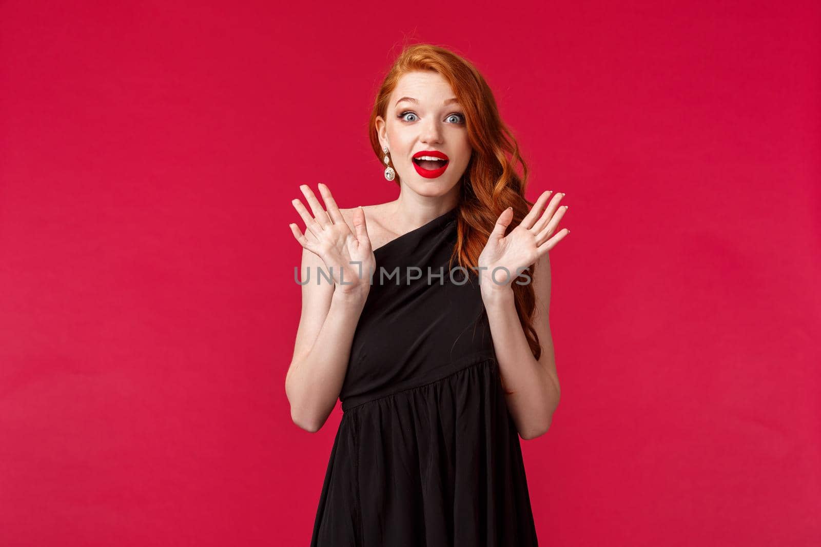 Fashion, luxury and beauty concept. Portrait of excited, overwhelmed young stunned redhead elegant woman in slim black dress, raising hands astonished and curious, look camera satisfied by Benzoix