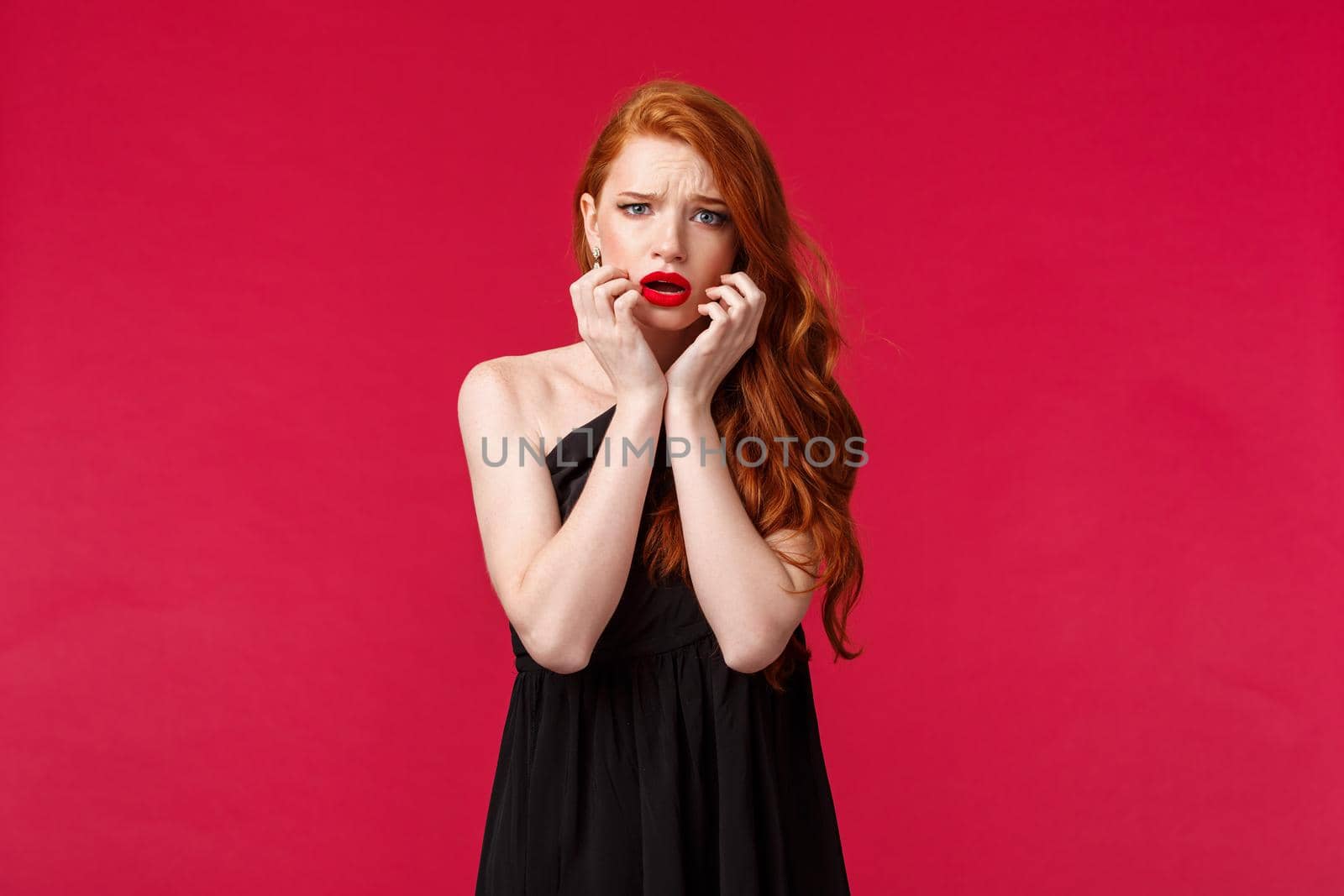 Fashion, luxury and beauty concept. Portrait of timid and scared ginger girl in black dress feel unsafe or insecure, touch face frowning frightened, look concerned and worried camera, red background by Benzoix