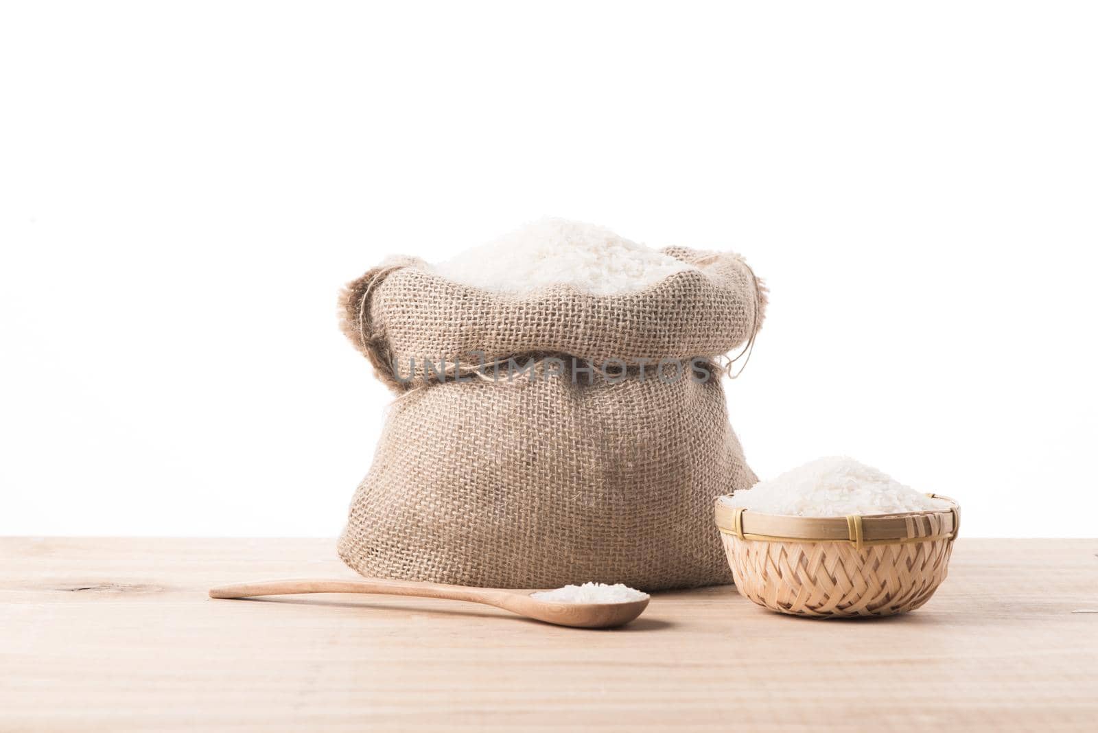 White rice in burlap sack and bowl on top of wooden table