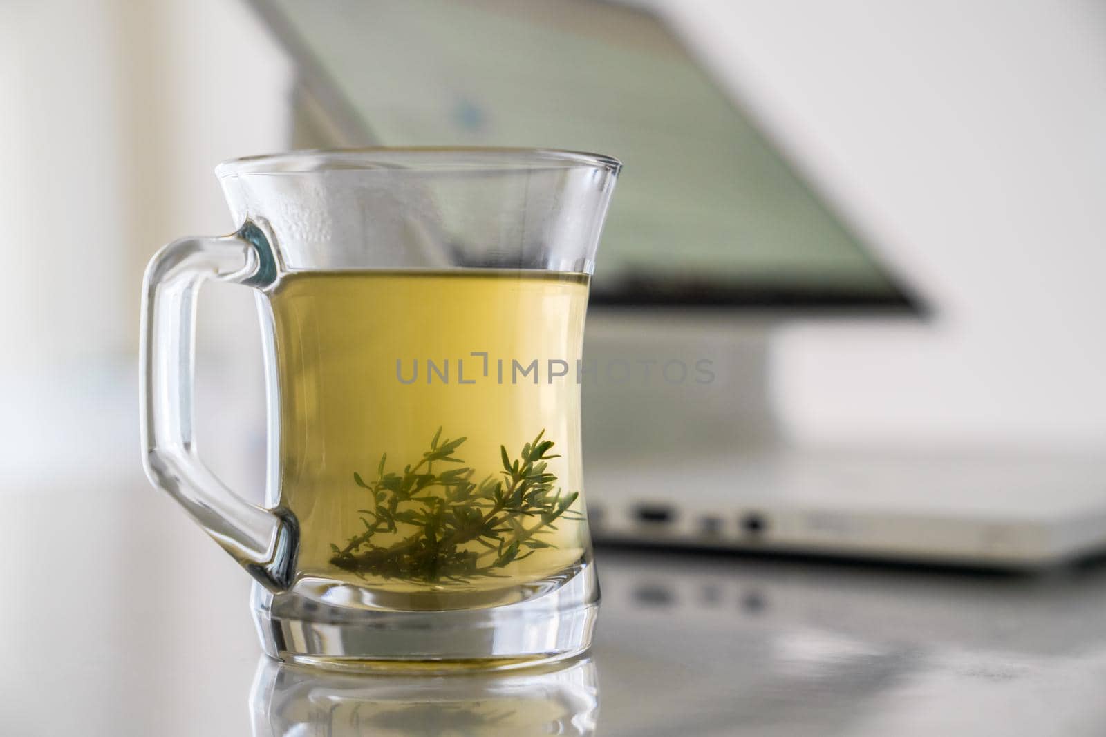Glass transparent cup with herbal tea with grass leaves on the background of a working computer. Concept of relax. by Laguna781