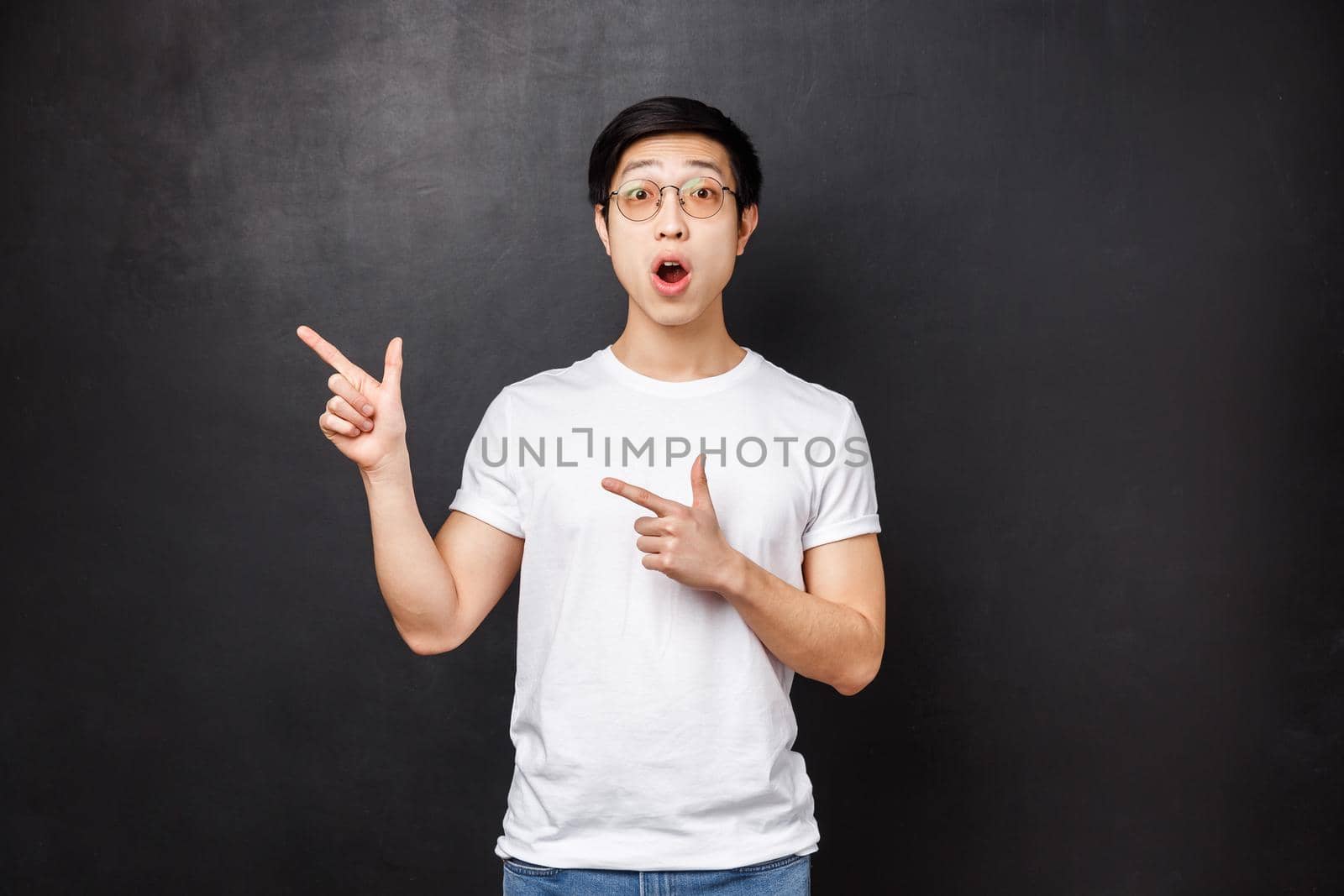 Portrait of surprised amazed young asian guy in white shirt react with disbelief and amazement at something unique and interesting written left, pointing upper corner gasping impressed.