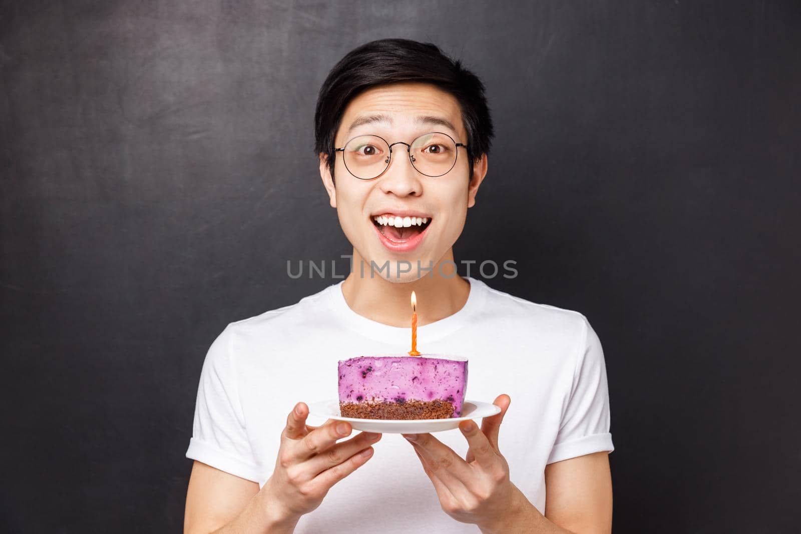 Celebration, holiday and birthday concept. Close-up portrait of amazed and happy young asian man holding b-day cake and smiling amused, throw party, blow out candle for making wish.