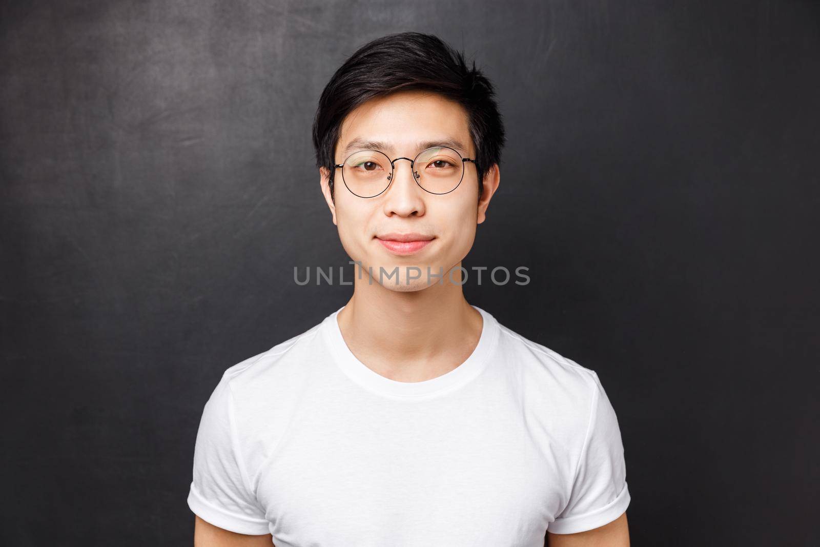Close-up portrait of simple cute asian man in white t-shirt and glasses, smiling at camera looking friendly and relaxed, posing over black background alone, lifestyle and people concept.