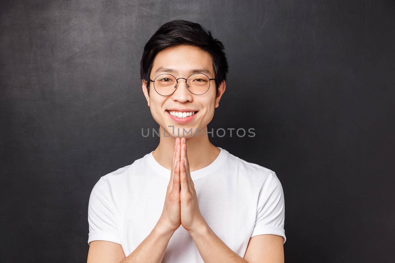 Close-up portrait of friendly, polite and relaxed young asian man with happy smile, hold hands in pray, palms pressed together over chest, smiling at camera, say namaste, praying.