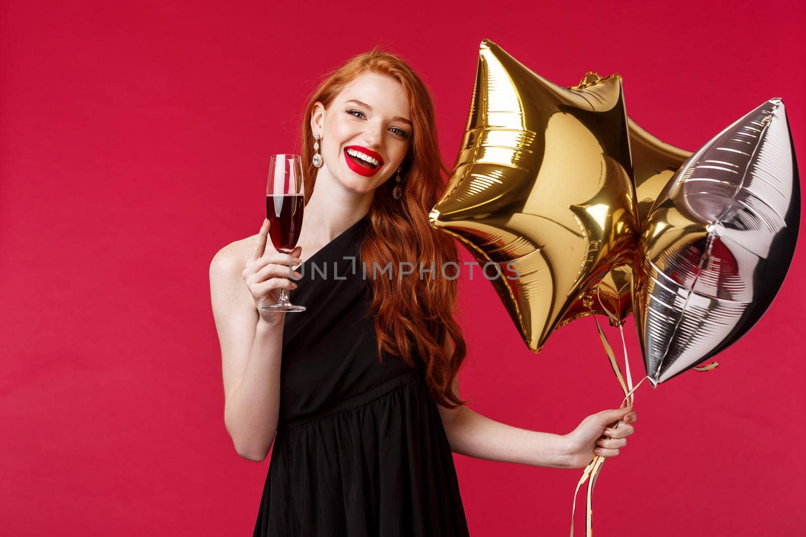 Portrait of happy carefree, gorgeous redhead woman in elegant black dress partying, saying toast, cheers holding glass of champagne or wine, smiling happy with balloons in hand, red background by Benzoix