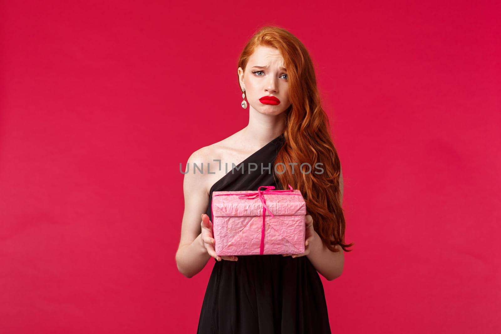 Celebration, holidays and women concept. Portrait of gloomy and upset birthday girl feel distressed and uneasy, holding one pink box with b-day gift, sobbing, no one came to party, red background.