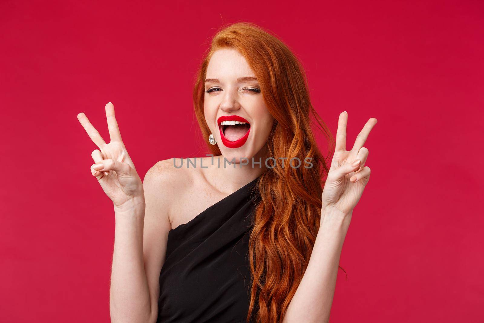 Close-up portrait of sassy and carefree redhead girl having fun, enjoying awesome party, show kawaii peace signs dancing joyfully, celebrating holiday in black dress and red lipstick.