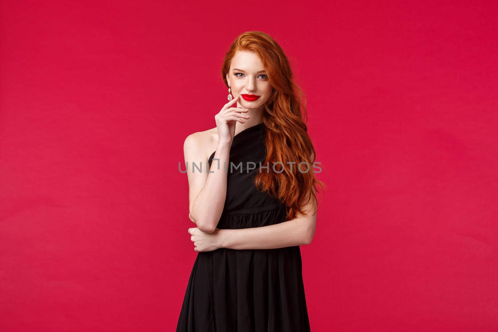 Elegance, fashion and woman concept. Portrait of seducative good-looking redhead woman in slim elegant black dress, red lipstick and evening makeup, look daring and sassy, red background by Benzoix
