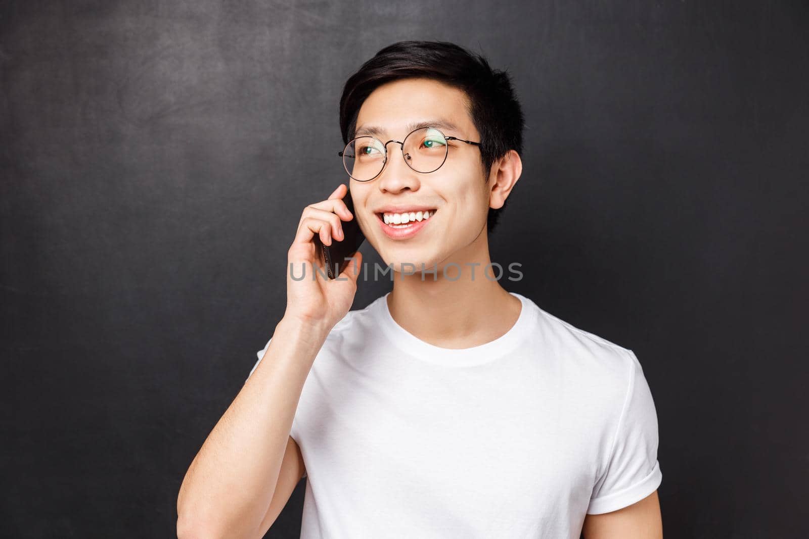 Technology, messaging and people concept. Close-up portrait of carefree asian guy in glasses, talking on phone, smiling and looking away while having conversation, call for appointment.