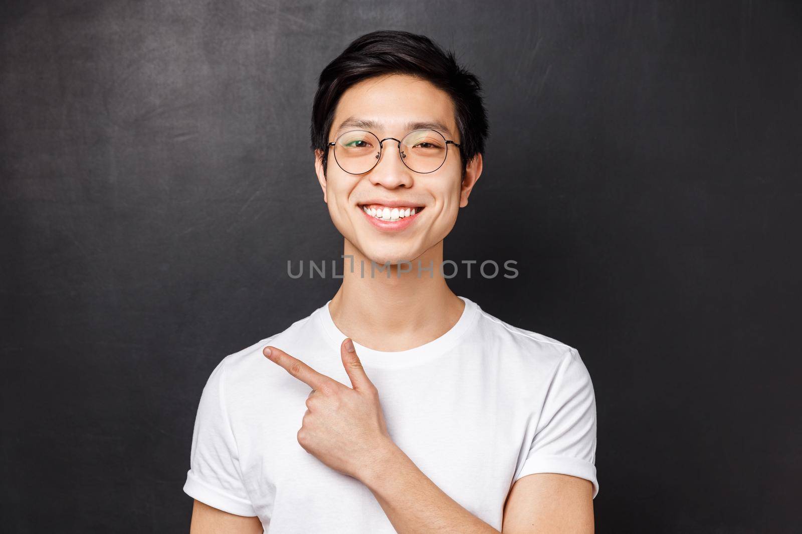 Close-up portrait of cheerful young adult guy start own business on internet platform, wearing glasses, pointing finger left and smiling, give recommendation, suggest visit webpage.
