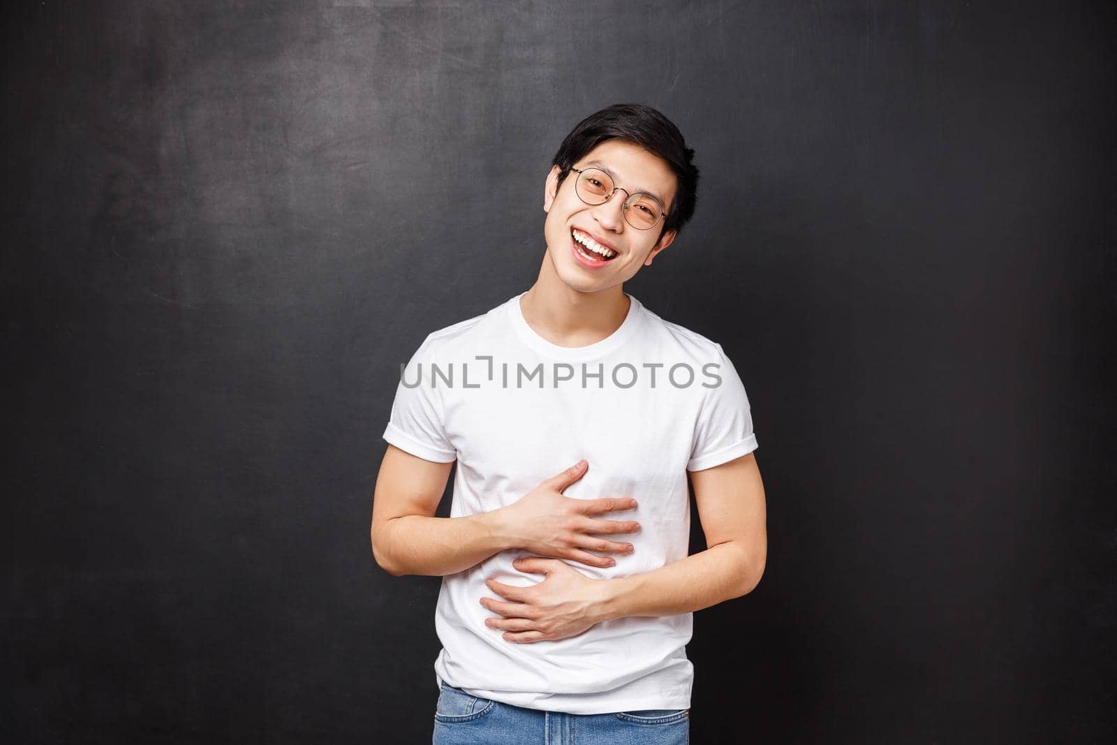Portrait of charismatic friendly asian guy in glasses and t-shirt, hang-out with friends, having fun, tilt head smiling and laughing, fill pain in stomach from chuckling at jokes, black background by Benzoix