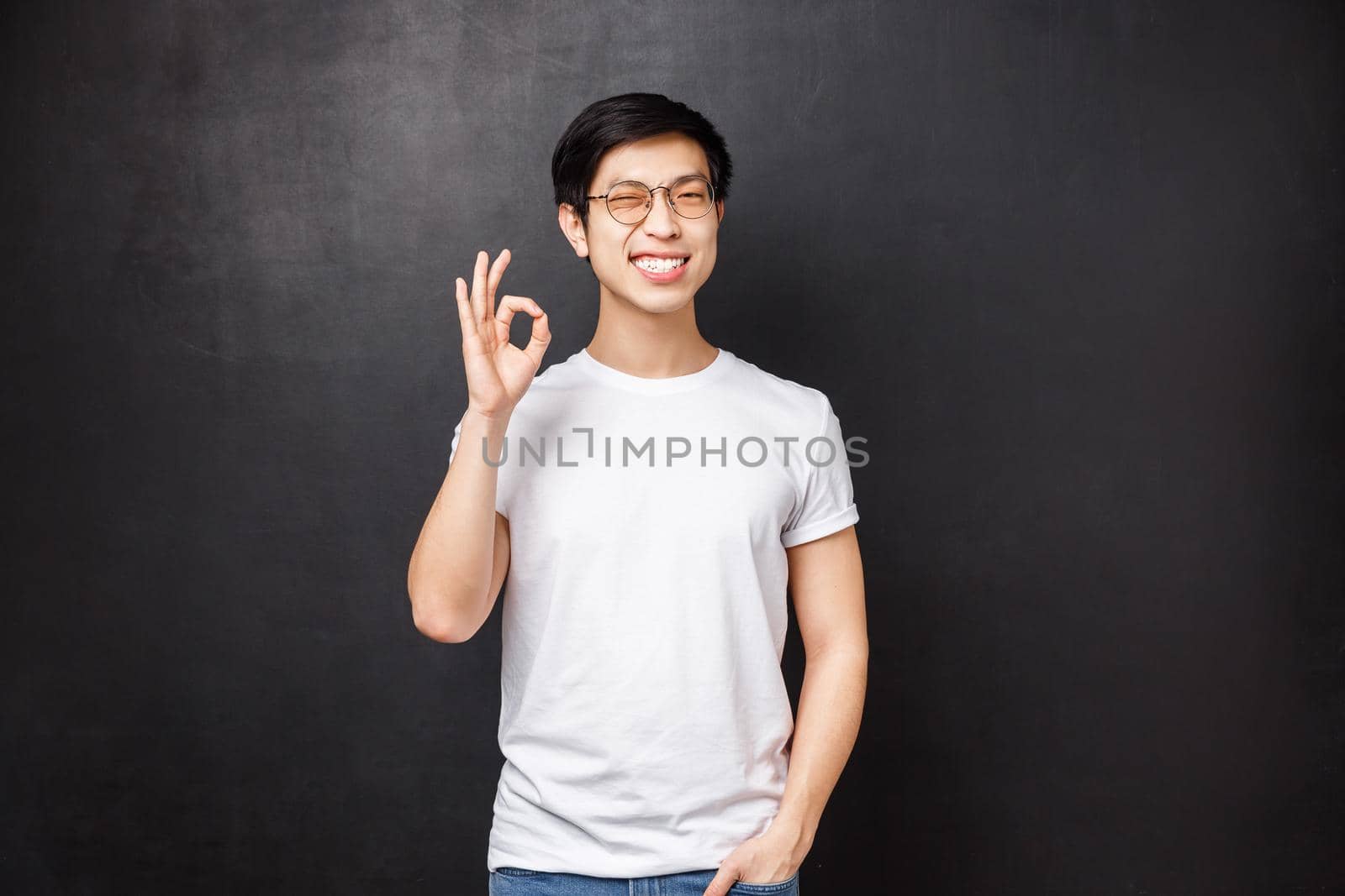 Carefree happy smiling young asian guy left satisfied after trying new product, visit company and use their good services, show okay sign and wink joyfully, pleased over black background by Benzoix