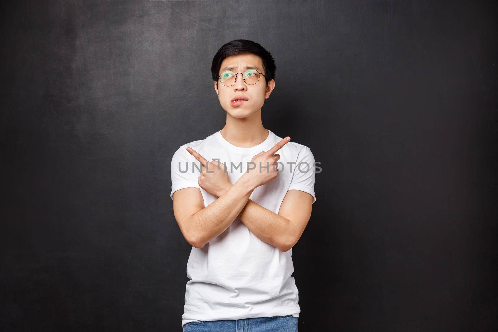 Indecisive silly asian guy dont know what choose, pointing fingers sideways left and right at two varitants or products, biting lip hesitant look away as thinking, making decision by Benzoix