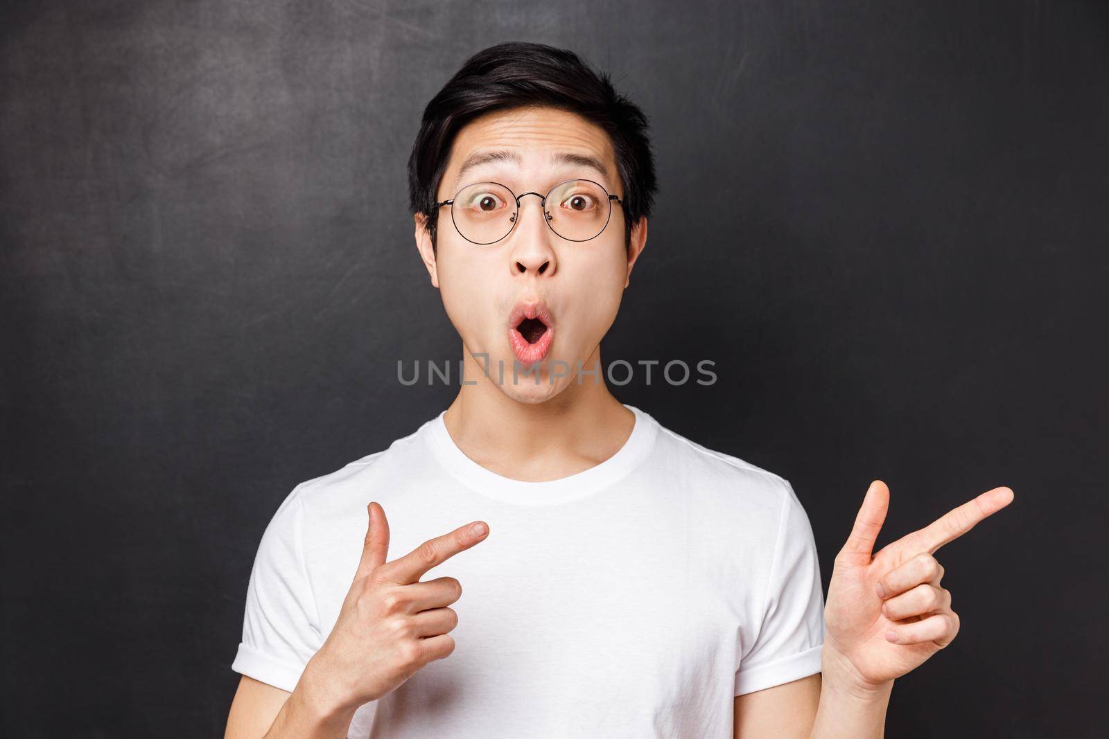 Close-up portrait of thrilled and amused asian young man in white t-shirt, open mouth amazed say wow, pointing fingers right at something impressive and stunning, white background by Benzoix