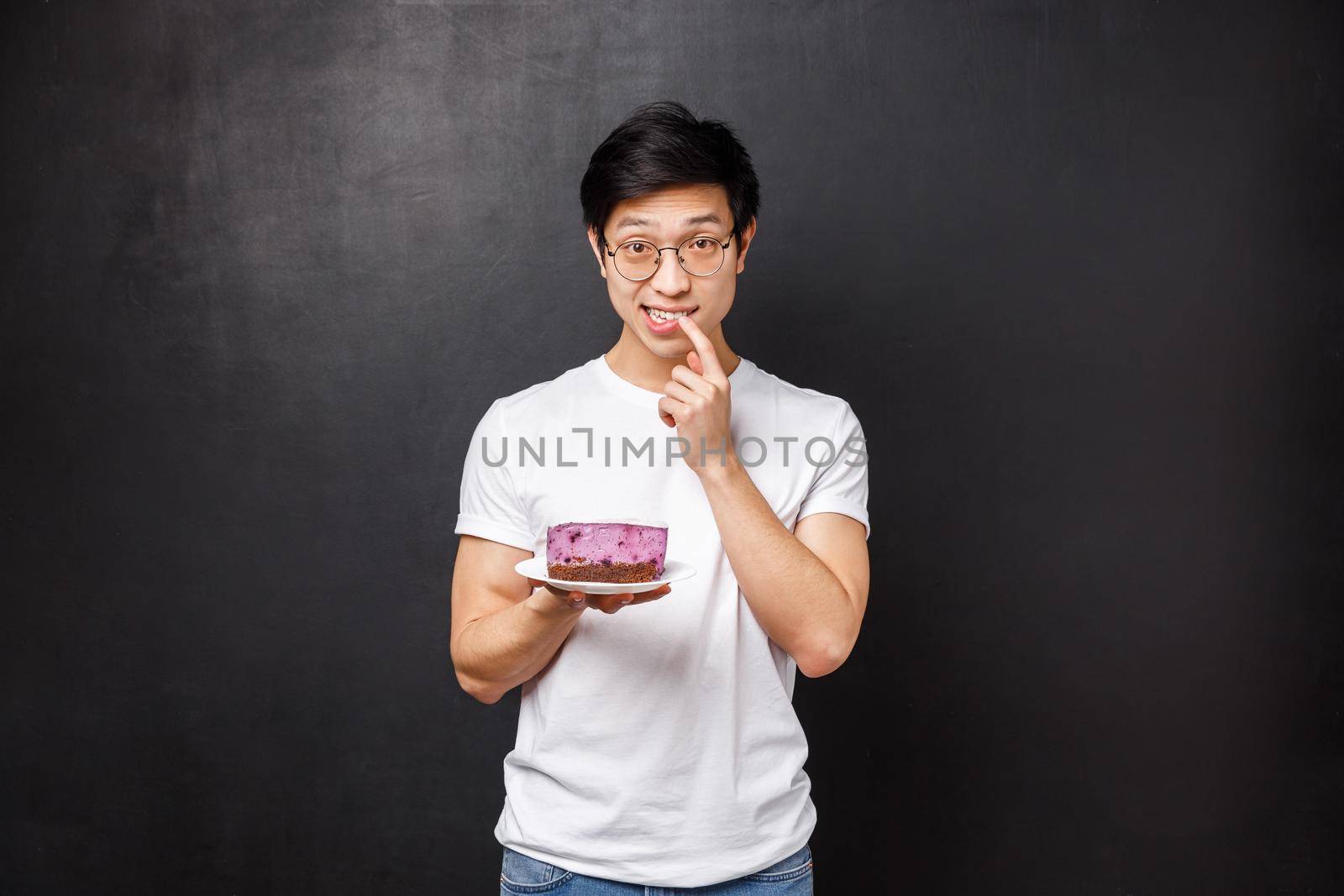 Potrait of shy and silly asian guy suggesting his piece of cake to girl he likes, asking try it as made dessert on his own, biting finger and look awkward at camera, asking your opinion by Benzoix