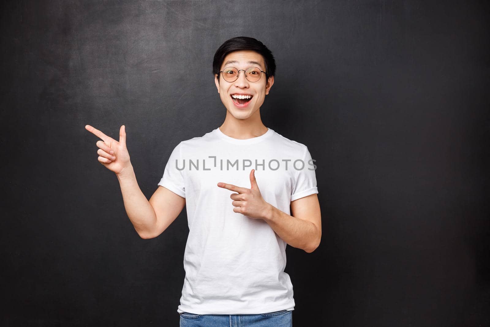 Happy cheerful smiling asian man feel excited, pointing fingers left and cheering found excellent opportunity apply for good job, dream career or company that help study abroad, black background.