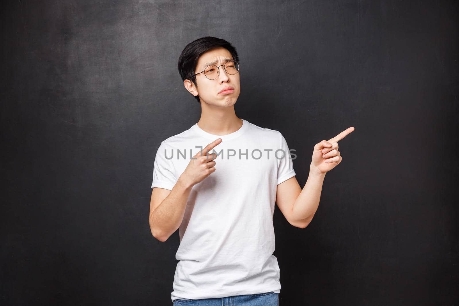 Portrait of skeptical and displeased young picky asian guy looking doubtful at product, being unsure in quality, pointing fingers right, squinting suspicious, having second thouhgts by Benzoix