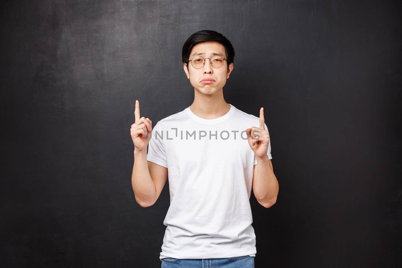 Portrait of gloomy and upset distressed young asian guy whining, complaining on unfair life, pointing fingers up with regret and jealous, look camera, cant afford too expensive product.