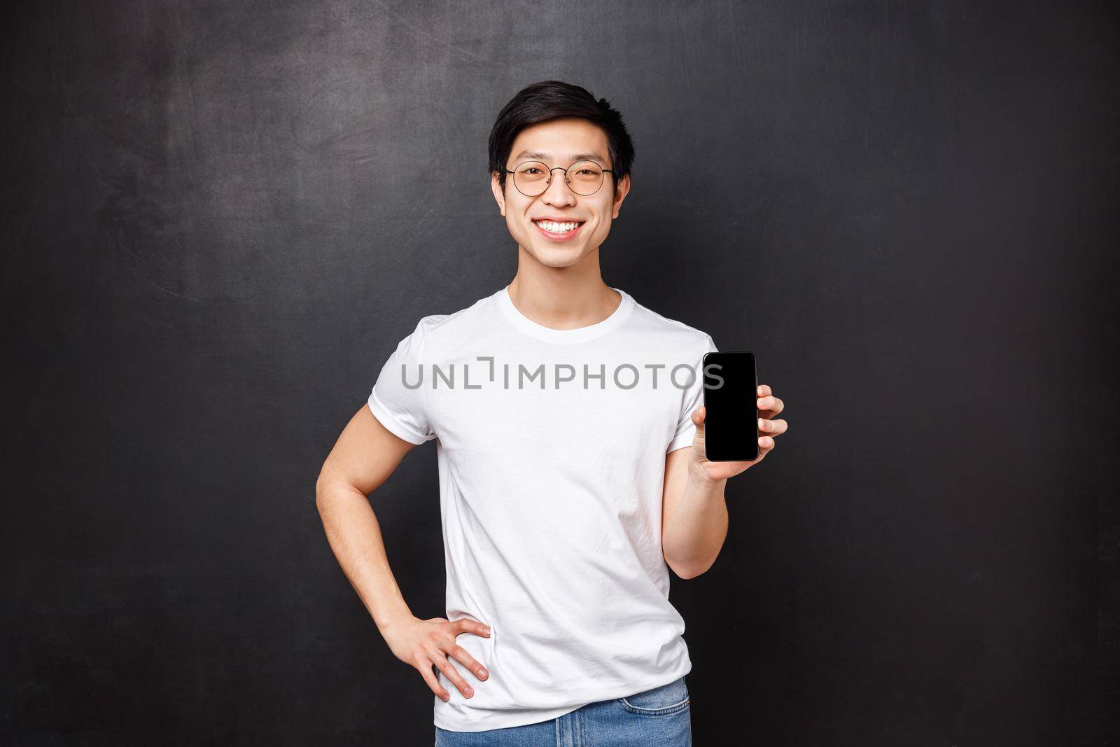 Technology, gadgets and people concept. Portrait of young male store clerk showing new features of smartphone, holding mobile phone and introduce application or company banner on gadget display.