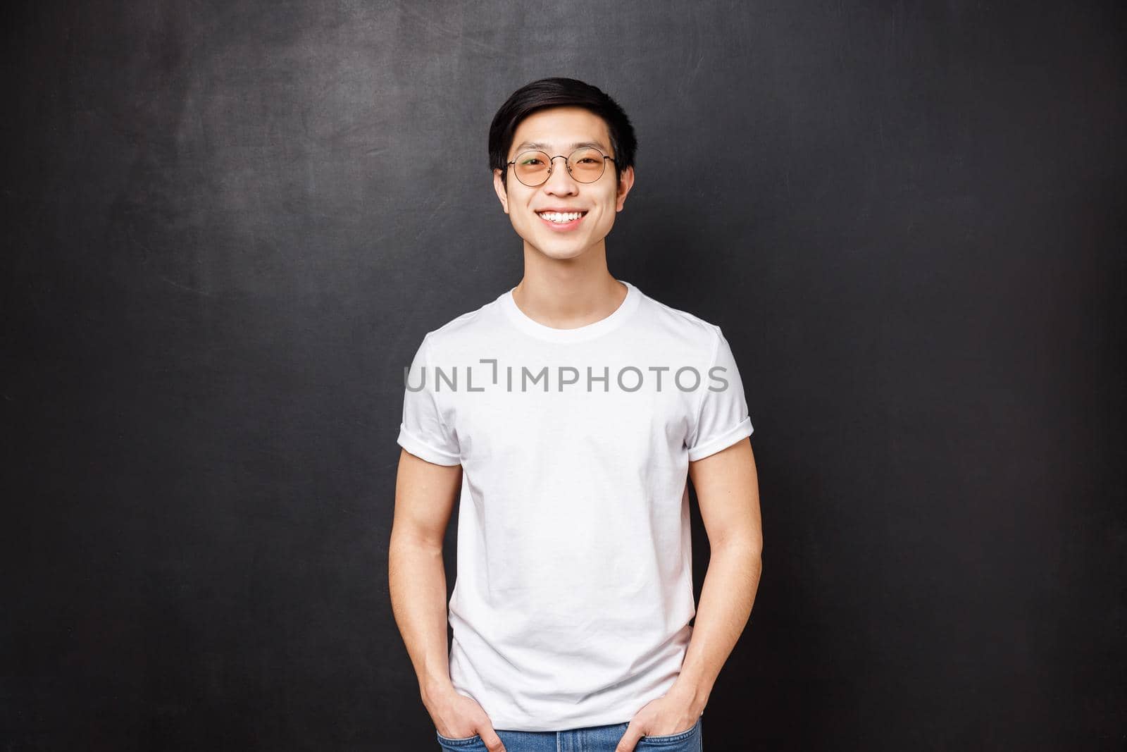 Portrait of young asian guy in glasses standing in white casual shirt over black background, friendly smiling, express happy enthusiastic emotion, hanging with mates after college.