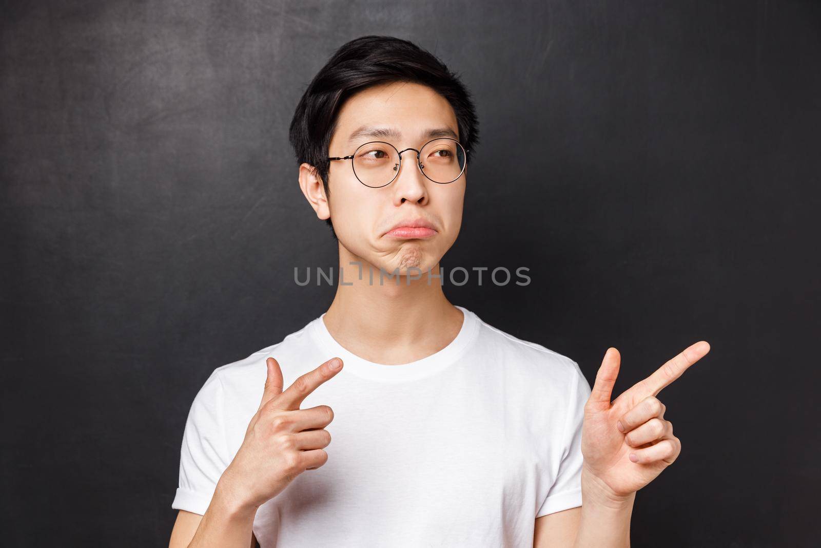 Not bad. Close-up portrait of impressed and curious young enthusiastic asian man in glasses and white t-shirt approve something good, pointing looking right, nod agreeting, black background.